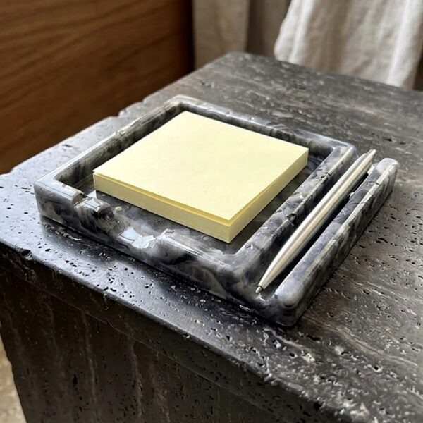rey marbled jesmonite desk tray holding a yellow sticky note pad and silver pen on a dark stone table