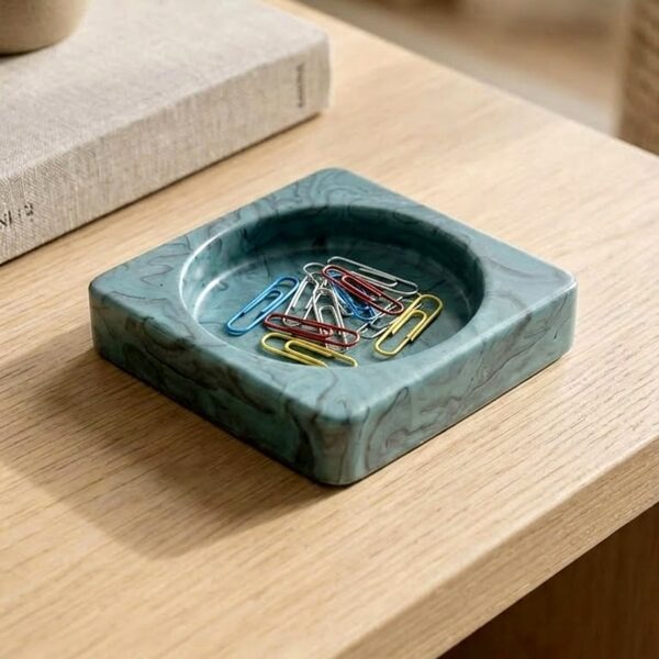 Teal marbled jesmonite square tray holding colourful paper clips on a light wooden desk